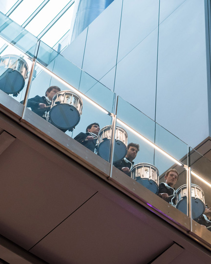 A group of percussion students drumming on a bridge, taken from below.